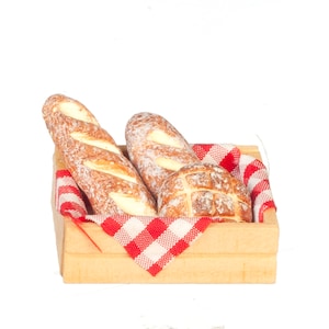 May include: A wooden crate filled with miniature bread loaves. Two baguettes and a round loaf are visible, resting on a red and white checkered cloth. The bread has a golden-brown crust.