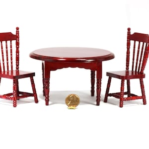 May include: Miniature dollhouse dining set with a round table and two chairs. The set is made of dark red wood. The table is approximately 3 inches in diameter. The chairs have a spindle back design.