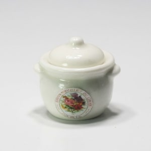 May include: A small, off-white ceramic pot with a lid. The pot has two small handles and a floral sticker that reads "SAVON BOUQUET DU LIBAN PARIS". The pot is likely a decorative item.