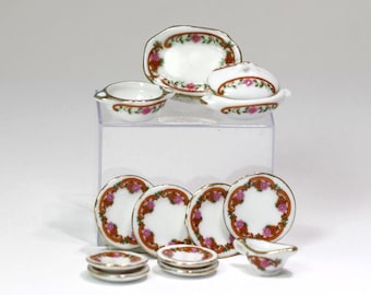 May include: A miniature porcelain tea set with a floral design. The set includes plates, bowls, and serving dishes with a white background, red and pink floral accents, and gold trim. The set is displayed on a clear acrylic stand.