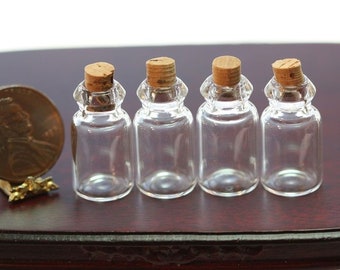 May include: Four small, clear glass bottles with cork stoppers. The bottles are lined up next to a penny for size comparison. The bottles have a decorative, rounded top. The penny is in a small gold-colored stand.