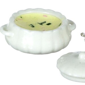 May include: A miniature white porcelain soup set. The set includes a soup tureen with a lid, two teacups with saucers, and two spoons. The soup appears to be a pale yellow color with green and pink accents.