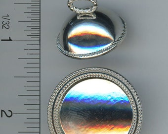 May include: Two silver-colored, round objects with a reflective surface. The top object has a loop and a rope-like border. The bottom object is a larger circle with a similar rope-like border. The objects are next to a ruler.