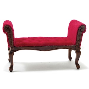 May include: Miniature red velvet bench with dark brown wooden frame and legs. The bench has a tufted seat and curved armrests with decorative carvings. A small-scale furniture piece, likely for a dollhouse or display.
