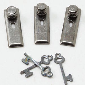 May include: Three silver-toned metal latches with a keyhole design and a small, round knob on top. Below, three small, decorative skeleton keys are arranged, with a classic bow and bit design.