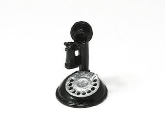 May include: A miniature black antique telephone with a silver dial. The rotary phone has a base, a central stem, and a receiver. The dial has finger holes around the perimeter. The phone is set against a white background.