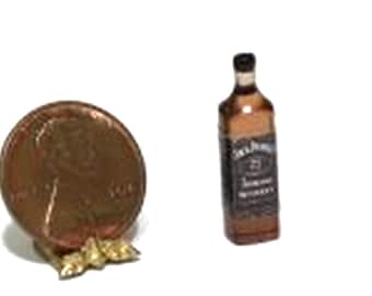 May include: Miniature whiskey bottle with a black label and a penny for scale. The bottle is brown with a black cap. The penny is copper-coloured and is next to a small gold-coloured object.