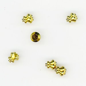 May include: A collection of small, gold-colored furniture knobs and a single flat-topped screw. The knobs have a decorative, tiered design. The items are arranged on a white surface.