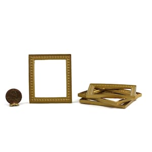 May include: A collection of small, gold-colored picture frames. One frame stands upright, while others are stacked. A penny is next to the upright frame for size comparison. The frames have a decorative beaded edge.