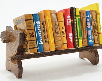 May include: A miniature wooden bookshelf filled with colorful, decorative books. The books have various spine colors, including yellow, blue, and red, with intricate gold and white detailing. The bookshelf is made of dark brown wood.