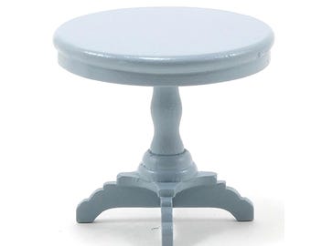 May include: A small, light blue, round table with a pedestal base. The table has a circular top and a decorative base with curved edges. The table is approximately 3 inches in diameter and 3 inches tall.