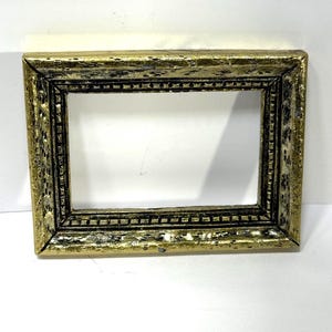 May include: A rectangular picture frame with a distressed gold finish. The frame has a detailed, textured design with black accents, and a rectangular opening in the center. The frame is set against a white background.