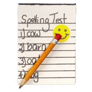 May include: A close-up of a spelling test on lined paper with the words "cow", "barn", "zoo", and "dog" listed. A yellow smiley face sticker is next to the test. A yellow pencil with a red eraser is resting on the paper.