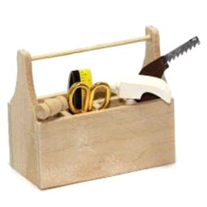 Puede incluir: Una pequeña caja de herramientas de madera con asa, que contiene pequeñas herramientas. Las herramientas incluyen una sierra, tijeras, una cinta métrica y un objeto blanco. La caja de herramientas es de madera clara.