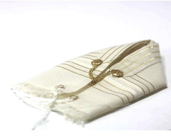 May include: Off-white scarf with gold stripes and fringe. The scarf is folded and secured with a gold-colored clasp and chain. The clasp has a floral design. The scarf is made of a soft, lightweight material.