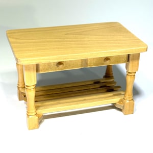 May include: A small, rectangular wooden table with a light finish. The table has two small drawers and a slatted shelf. The legs are turned and have a decorative shape. The table is approximately 12 inches long, 8 inches wide, and 6 inches tall.