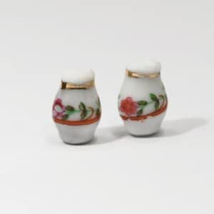 May include: Two small, white ceramic salt and pepper shakers. Each shaker has a gold rim and a floral design featuring red roses and green leaves. A thin orange band encircles the base of each shaker.