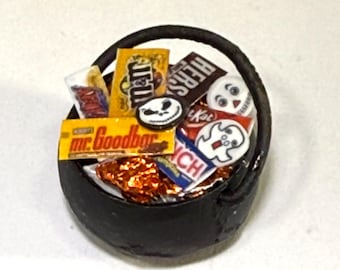 May include: A miniature black cauldron filled with assorted tiny candy bars and Halloween-themed decorations. The collection includes miniature replicas of Mr. Goodbar, Hershey's, and Crunch wrappers, alongside small ghost and skull-shaped charms.