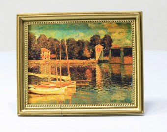 May include: A framed print of a waterscape with boats, trees, and buildings. The artwork is in a gold-colored frame. The print depicts a serene scene with reflections in the water, and the colors are muted with a vintage feel.