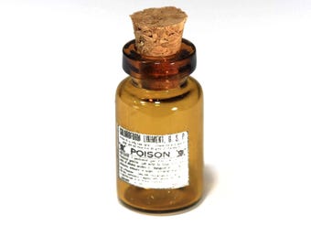 Puede incluir: Una pequeña botella de vidrio ámbar con tapón de corcho. La botella tiene una etiqueta con la palabra "POISON" y otro texto. Es probable que sea un artículo antiguo, posiblemente para almacenar medicamentos o productos químicos.