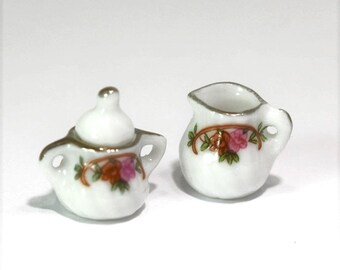May include: Miniature white porcelain tea set with gold trim. The set includes a teapot with a lid and a creamer, both decorated with floral designs in pink, orange, and green.