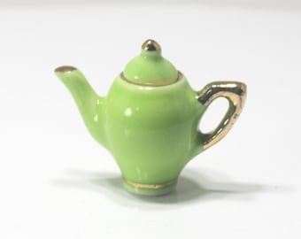 May include: A small, lime green ceramic teapot with gold trim. The handle, spout, and lid are accented with gold. The teapot has a glossy finish and a small, rounded lid with a gold knob. A miniature decorative item.
