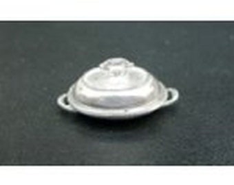 May include: A small, silver-colored dish with a lid and two small handles. The lid has a decorative knob on top. The dish is round and appears to be made of metal. The background is a dark color.