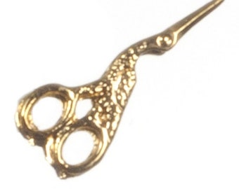 May include: A small, ornate gold-colored pair of scissors. The scissors have a detailed, textured pattern on the handles and a pointed blade. The design suggests a vintage or antique style, suitable for crafting or sewing.