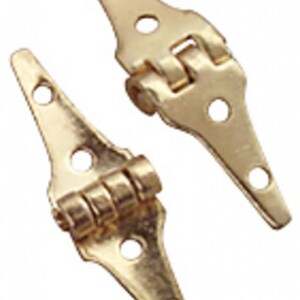 May include: Two gold-colored hinges with a decorative shape. Each hinge has three holes for screws and a folding joint in the center. The hinges are made of a shiny, metallic material.