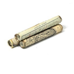 May include: Three rolled vintage-style maps with aged paper texture. The maps are beige and cream-colored, with black and brown illustrations and text. One map has the text "SCUTER-INDIE".