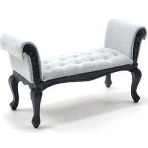 May include: Miniature chaise lounge with a tufted, light gray seat and backrest. The frame and legs are black, with ornate detailing on the arms and legs. A small, decorative furniture piece.