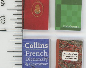 May include: Four miniature books are displayed. A red book with a gold framed portrait, a green notebook with "NoteBook" and "Clairefontaine" text, a blue "Collins French Dictionary & Grammar", and a marbled cover book.