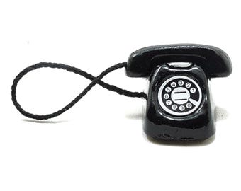 May include: A miniature black rotary phone with a white dial and numbers. The phone has a curved handset and a coiled cord. The phone is a vintage-style decorative item.