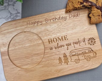 May include: Wooden serving board with a circular indentation and the engraved text "Happy Birthday Dad!" and "HOME is where you park it" with a camper van illustration. A chocolate chip cookie rests on the board.