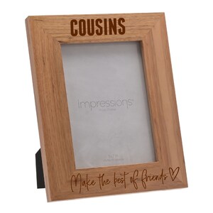 Puede incluir: Un marco de fotos de madera con las palabras "COUSINS Make the best of friends" grabadas en él. El marco es marrón y tiene una abertura de 13x18 cm.