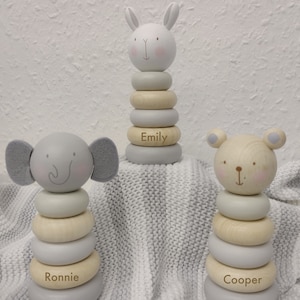 May include: Three wooden stacking toys shaped as an elephant, a bunny, and a bear. Each toy has a stack of rings in neutral colours, with the names "Ronnie", "Emily", and "Cooper" engraved on the base ring.