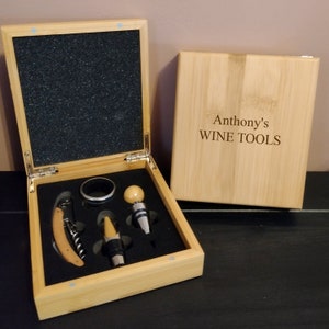 May include: A wooden box with a black interior and a set of wine tools. The box is open and the tools are visible. The tools include a corkscrew, a bottle stopper, and a ring pull. The box is labelled "Anthony's WINE TOOLS".