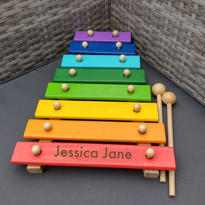 Op de afbeelding: Een regenboogkleurig houten xylofoon met twee houten hamers. De xylofoon heeft een gepersonaliseerde inscriptie met de tekst "Jessica Jane".