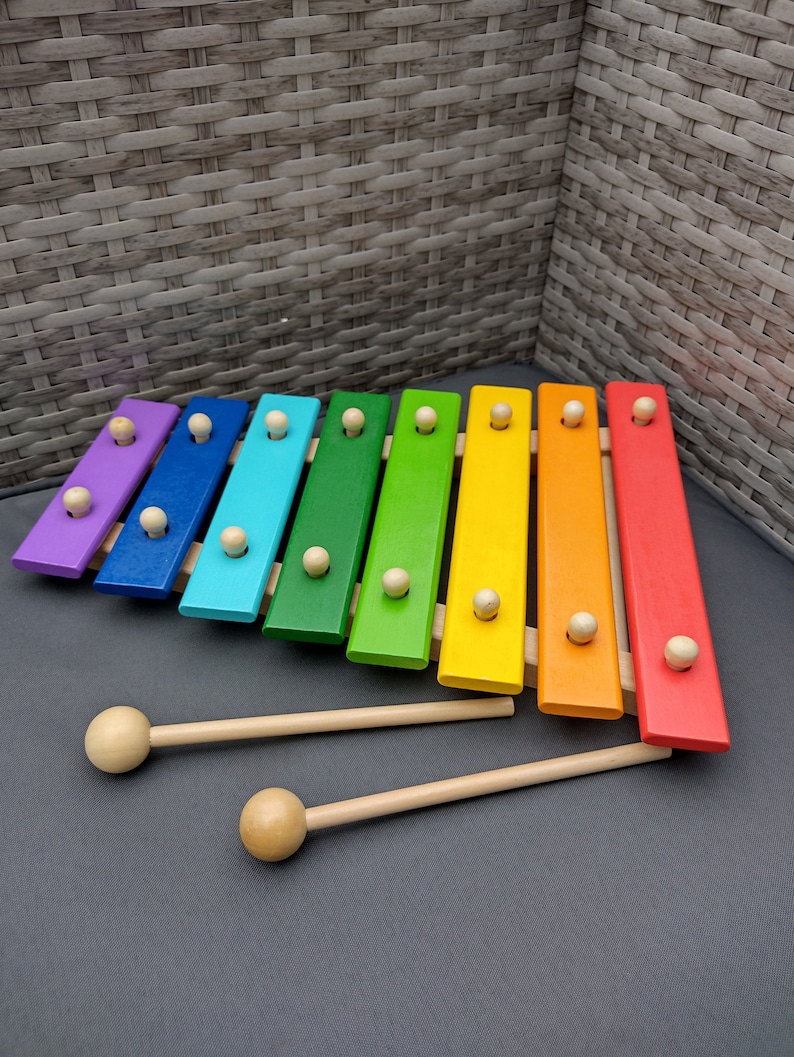 Op de afbeelding: Een regenboogkleurig houten xylofoon met twee houten hamers. De xylofoon heeft acht toetsen en is gemaakt van verschillende soorten hout.