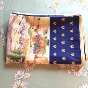 May include: Folded silk scarf with a floral and landscape design. The scarf features a section with a blue background and gold floral accents. The other sections have a cream background with purple, orange, and green floral and landscape designs.