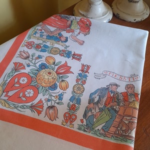 May include: White tablecloth with a red and orange border. The tablecloth features a colorful floral design with a central heart motif. The text "FESSTIA" is visible in the upper right corner.