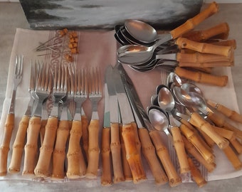 May include: A set of silverware with bamboo handles. The set includes forks, knives, and spoons. The silverware is arranged on a white cloth.