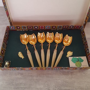 May include: Set of six gold-tone melon spoons with ivory-colored handles in a box with a green interior and a colorful patterned exterior. The box has a label that says "Speciale Melons".
