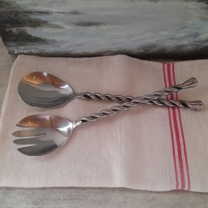 May include: A set of silver salad serving utensils with twisted handles. The utensils are on a white linen napkin with red stripes.