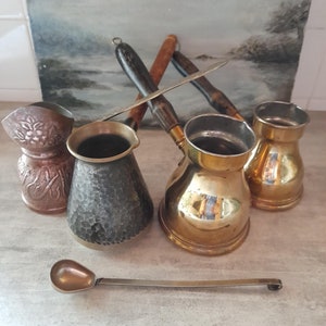 Peut inclure: Ensemble de quatre cafetières turques vintage, comprenant une petite cuillère de service. Les pots sont en laiton et en cuivre avec des finitions martelées. Un pot est noir avec une finition martelée, un autre est en cuivre avec un motif floral et deux sont en laiton avec une finition brillante.