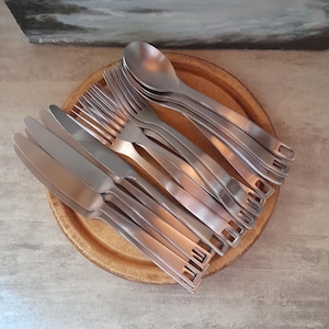 Pode incluir: Um conjunto de talheres de aço inoxidável, incluindo garfos, facas e colheres, cuidadosamente dispostos em uma bandeja de madeira. Os talheres estão empilhados em um padrão circular, com as alças voltadas para fora.