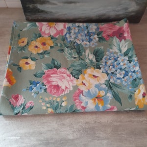 May include: A green fabric with a floral pattern featuring pink, yellow, and blue flowers. The fabric is folded in half and lying on a gray surface.