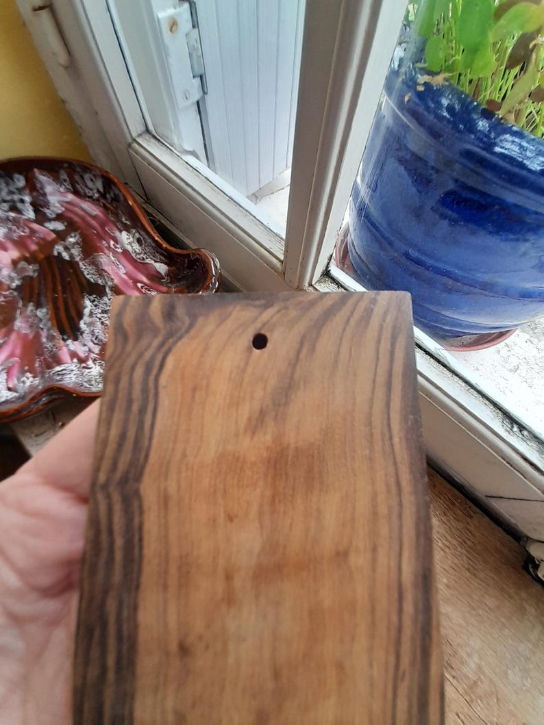 May include: A rectangular wooden cutting board with dark brown and light brown wood grain. The board has a small hole in the top center.