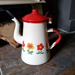 May include: White enamel teapot with a red lid and a floral design featuring red, yellow, and green flowers. The teapot has a white handle and a spout.