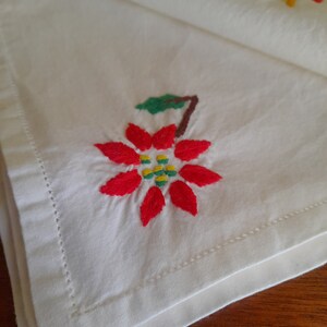 Op de afbeelding: Witte linnen servet met een geborduurde kerstster bloem in rood, groen en geel.